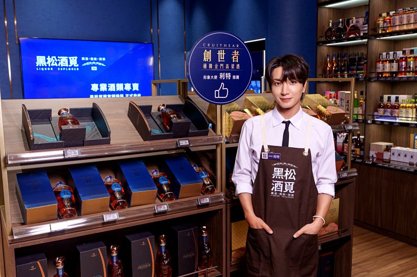 利特身穿工作圍裙於店內陳列區與「創世者」酒款合影展現親切形象。