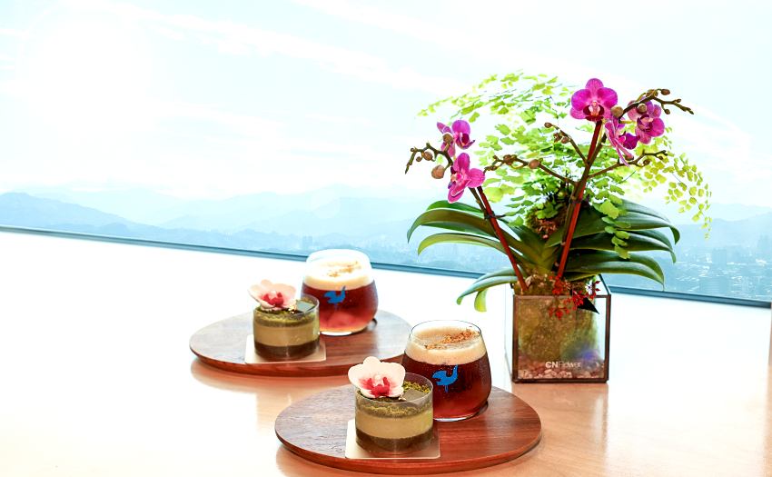 台北101攜手kafeD推出觀景台限定新品，包含金桂愛玉耶加雪菲與擂茶巧克力蘭花蛋糕，讓遊客佐以高空美景享受味覺療癒。
